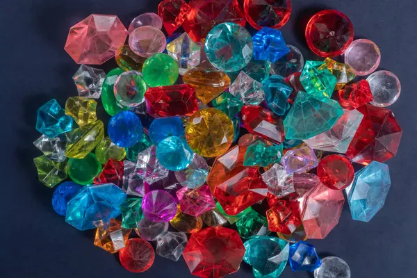 Çok renkli değerli taşlar ve cam kristallerden oluşan çarpıcı bir düzenleme canlı renkler sergiliyor ve koyu arkaplana karşı parıldayan tasarımlar sergiliyor..