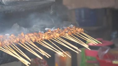 Geleneksel kömür ateşinde tavuk satay. Duman ve iştah açıcı bir bakışla alev alev yanıyordu. Eller ızgarada satay pişiriyor.