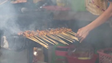 Geleneksel kömür ateşinde tavuk satay. Duman ve iştah açıcı bir bakışla alev alev yanıyordu. Eller ızgarada satay pişiriyor.