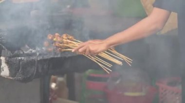 Geleneksel kömür ateşinde tavuk satay. Duman ve iştah açıcı bir bakışla alev alev yanıyordu. Eller ızgarada satay pişiriyor.