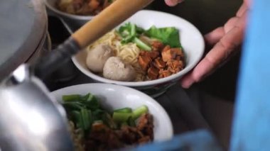 Tavuklu erişte hazırlıyorum. Penjual mie ayam bakso ya da alıcıya tavuklu erişte yapan köfteli tavuklu erişte satıcısı manzarası. Seçici odak. 