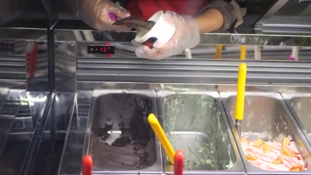 スクープ付きの女性の手は 冷蔵庫からアイスクリームを取り カップで提供しています おいしいアイスクリームのスクープを取る女性 アイスクリームと冷蔵庫 女性はアイスクリーム店で働いています ペストリーショップ デザート — ストック動画