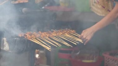 Geleneksel kömür ateşinde tavuk satay. Duman ve iştah açıcı bir bakışla alev alev yanıyordu. Eller ızgarada satay pişiriyor.