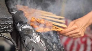 Geleneksel kömür ateşinde tavuk satay. Duman ve iştah açıcı bir bakışla alev alev yanıyordu. Eller ızgarada satay pişiriyor.