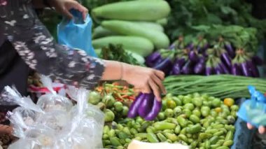 Satıcının markette sebze seçip plastik torbaya koyduğu yan görüş. Kadın sebze seçiyor ve tezgaha ekliyor.