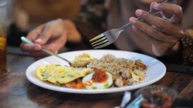 Bir restoranda kaşık ve çatalla kızarmış pirinç yiyen Endonezyalı bir kadın veya Nasi Goreng (Endonezyalı)