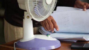 Endonezyalı bir kadının eli, ofisteki yüksek sıcaklıklara adapte olmak için modern bir yelpazeyi açıyor..