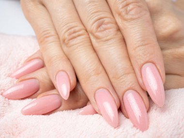 Modayı takip eden genç bir kadın beyaz arka planda pembe manikür yapıyor.