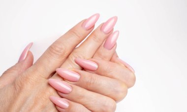Modayı takip eden genç bir kadın beyaz arka planda pembe manikür yapıyor.