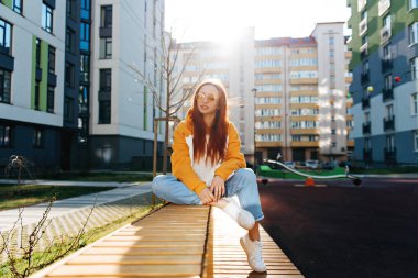 Rahat kızıl kız bankta oturuyor ve evinin yanındaki yaz güneşinin tadını çıkarıyor. İnsanlar ve doğa kavramı