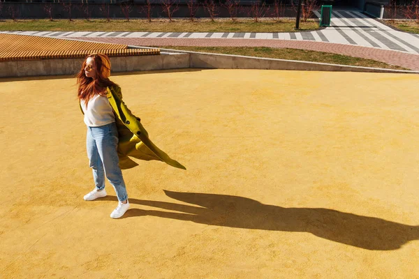 全景的姜汁女人穿着时髦的外套在城市体育场摆姿势 红头发的女孩戴着太阳镜站在街上欣赏阳光 — 图库照片