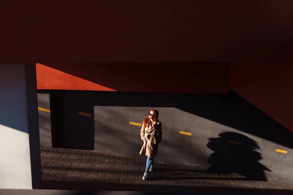 現代の女性の大まかな通りの壁に対してポーズ 通りに立つ都会の服のスタイルでサングラスの生姜の女の子 — ストック写真
