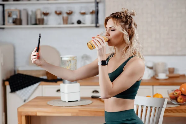 健康的な食事についてのビデオを撮影するために現代のスマートフォンを使用して細い体を持つかなり若い女性 ハッピーブロンド座っています椅子とホールディングガラスとともに新鮮なフルーツカクテル — ストック写真