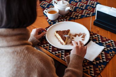 Tahta masada duran beyaz tabakta tiramisu yiyen kimliği belirsiz kadın. Kafe arka planı. Gıda ve restorasyon konsepti