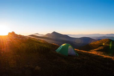Dağın tepesinde yeşil kamp çadırı ve arka planda muhteşem bir gündoğumu. Temiz hava için zaman harcamak. Seyahat konsepti.