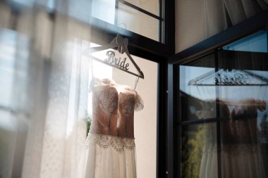 Gelin için beyaz gelinlikli ahşap askıyı kapat. Vitrinde şık kıyafetler asılı. Hazırlık sırasında ayrıntılar.