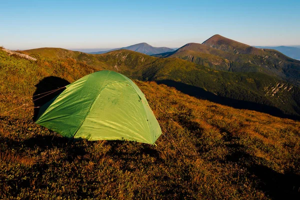 Dağın tepesinde yeşil kamp çadırı ve arka planda muhteşem bir gündoğumu. Temiz hava için zaman harcamak. Seyahat konsepti.