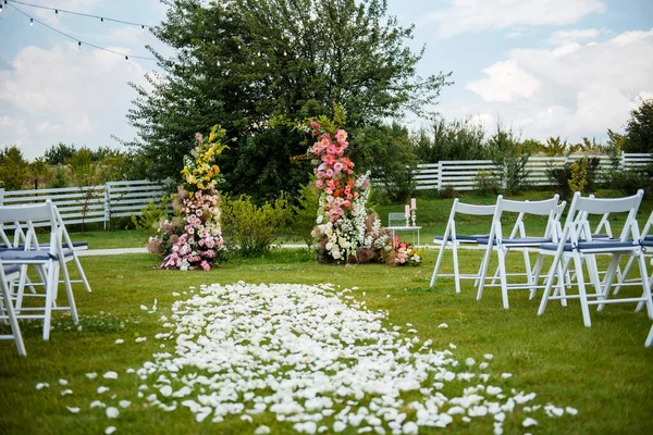 漂亮的拱门装饰着五彩缤纷的花朵 为大自然的婚礼做准备 新郎和新娘的时髦地方 客人用的白色椅子站着 — 图库照片