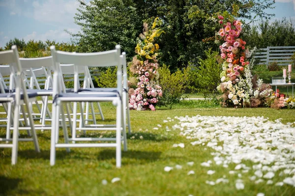 露天婚礼 拱门由五彩缤纷的花朵组成 中间是白色的木制椅子 两边站着 美丽的自然新郎和新娘区域 — 图库照片