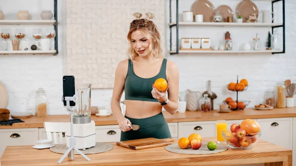 フィットネスブロガーは 健康的な食事についてモバイルでビデオを記録します 魅力的な強い女性で緑のスポーツ衣装記録ビデオのモバイル約健康食品 — ストック写真