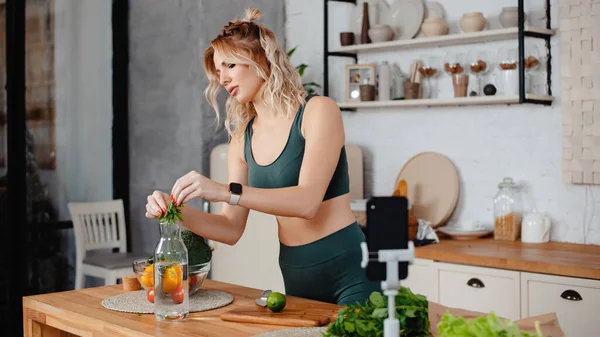 Fokuserad Blond Fitness Bloggare Förbereda Lemonad Samtidigt Spela Video Smartphone — Stockfoto