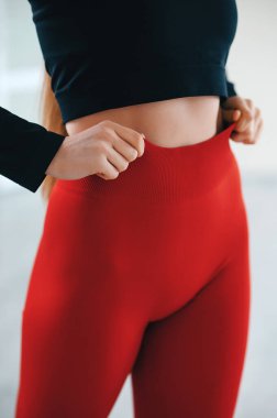 Beyaz stüdyo arka planında poz veren ve rahat giyinen kadın modelin yakın görüntüsü. İnce siyah üst ve dar kırmızı taytlar içinde mükemmel bir vücut manzarası.