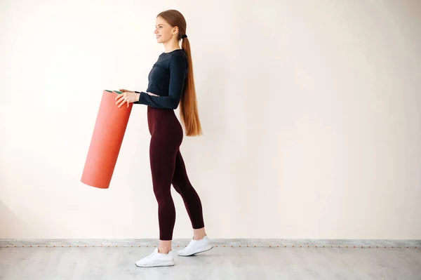 全身上下站着一个带着瑜伽垫的健身室 满面笑容的健身女人 一个年轻女子在健身训练中心的画像 — 图库照片
