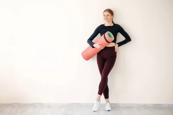 全身上下站着一个带着瑜伽垫的健身室 满面笑容的健身女人 一个年轻女子在健身训练中心的画像 — 图库照片
