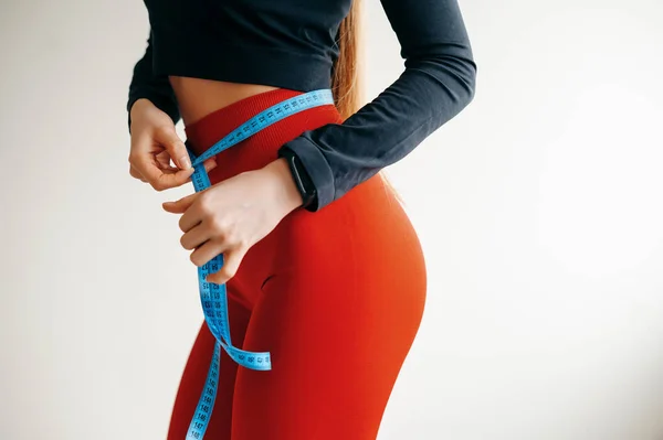 測定テープで腰を測定する女性の手のビューを閉じます 赤いパンツのレギンスと黒の上に女性の体を形成します スポーツ フィットネス 健康の概念 スペースのコピー — ストック写真