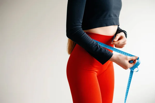 測定テープで腰を測定する女性の手のビューを閉じます 赤いパンツのレギンスと黒の上に女性の体を形成します スポーツ フィットネス 健康の概念 スペースのコピー — ストック写真
