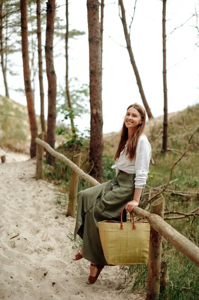 下午在沙滩小径上散步时 坐在木制篱笆上的愉快的快乐女人的画像 积极的女性 头戴草袋 看着相机 面带微笑 — 图库照片