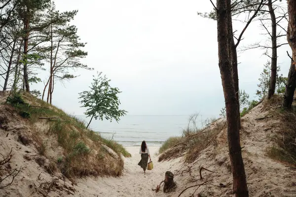后视镜 长发黑发女人穿过森林里的沙地小径去海滨 年轻的女士一个人在空旷的风景如画的地方消磨时光 沉默和放松的概念 — 图库照片