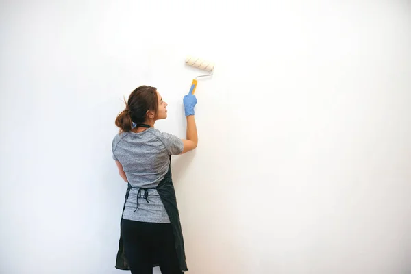 Young brunette woman painting walls with a roller in a new house. Interior design. Renovation. Rear view