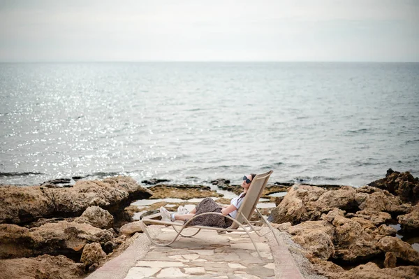 戴着太阳镜 穿着夏衣 躺在波涛汹涌的大海边的石子中的快乐而轻松的女人 人员和度假概念 — 图库照片