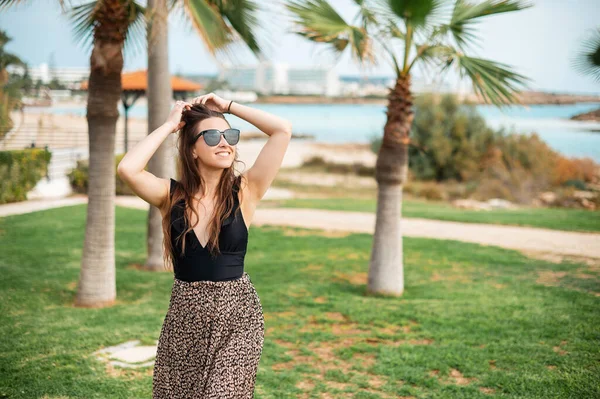 在豪华酒店附近的棕榈树旁 一个穿着时髦衣服 戴着太阳镜的美丽的高加索女人的近照 暑假的乐趣 — 图库照片