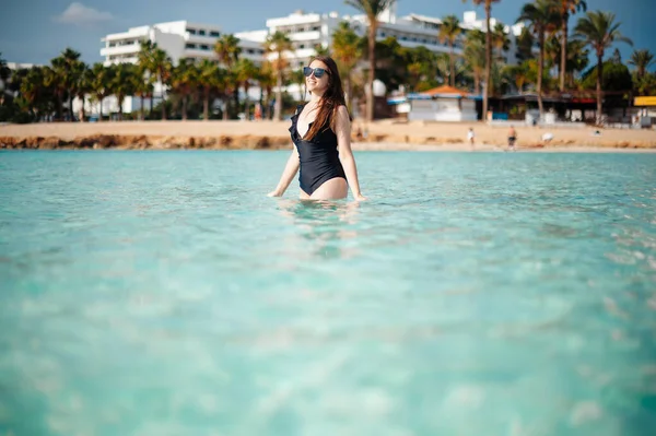 Güzel, siyah mayo ve güneş gözlüğü takan, yaz günü denizde ferahlatan beyaz bir kadın. Arka planda Ayia Napa şehri. Kıbrıs 'ta tatil zamanı