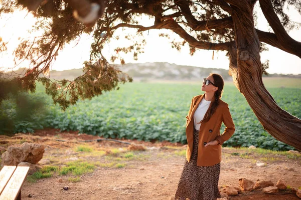 在塞浦路斯 迷人的高加索女人戴着时髦的太阳镜 穿着时髦的衣服 站在恋人的树下 参观历史名胜古迹 度假和旅行概念 — 图库照片