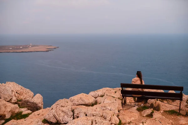 一个黑发女子坐在木制长椅上 欣赏岩石上美丽的海景的背景 度假期间迷人的夏季风景 — 图库照片