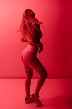 Back rear view of beautiful sexy blonde woman in beige underwear posing isolated in red neon light