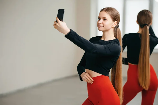 笑着纤细的女人 长长的秀发蓄成马尾辫 在手机上自拍 漂亮的女性在健身中心锻炼 并使用创新技术 室内培训 — 图库照片