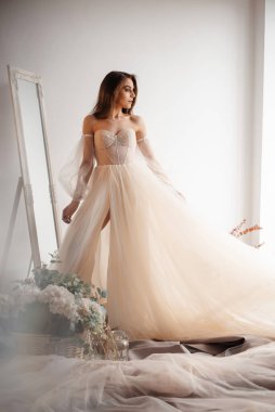 Gelinin sabahının romantik atmosferi. Şampanyanın renginde gelinlik giymiş nazik gelin pencereden dışarı bakar. 