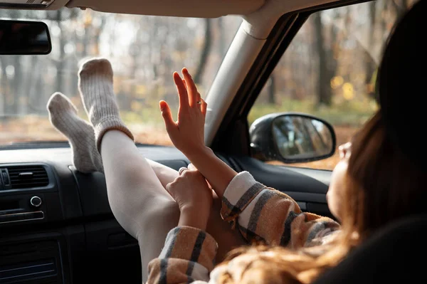 Modern arabanın içinde yardımcı sürücü koltuğunda oturan zarif bir kadın. Bacaklarını gösterge paneline koyuyor. Huysuz günün tadını çıkarıyor. 