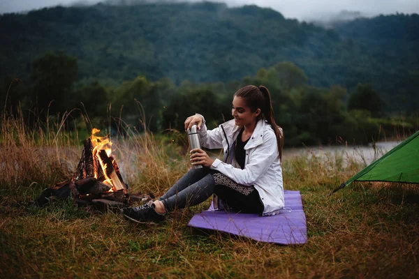 Счастливая Молодая Женщина Наливает Чай Термоса Сидя Рядом Горящим Огнем — стоковое фото