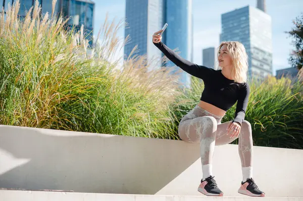 Fitness lady making selfie using mobile outdoors. Athlete woman in sportswear relaxing after workout at the street