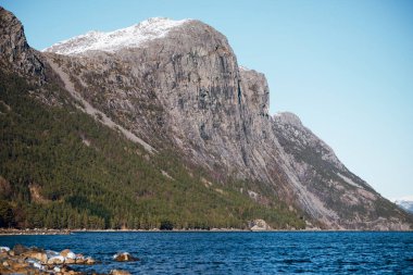 Soğuk mavi denizin manzarası ve kar zirveleri olan güzel dağlar. Taşlı nehir kıyısında. Norveç, Fjord 'da güneşli bir gün.