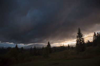 Yaz boyunca yeşil görkemli dağların üzerinden gökyüzünü kaplayan sağanak yağmurlu bulutlar. Vahşi doğada karanlık soğuk hava. Uzakta güneş ışığı.