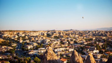 Türkiye 'de kayalık dağlar arasında inşa edilmiş eski köyün panoramik manzarası. Güneş ışığıyla harika bir mavi gökyüzü. Uzaktan uçan birkaç hava balonu..