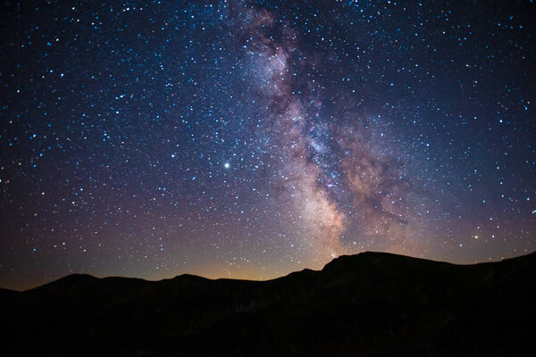 Светящиеся звезды на вечернем небе над горными вершинами. Захватывающий вид на природный узор. Волшебная атмосфера.