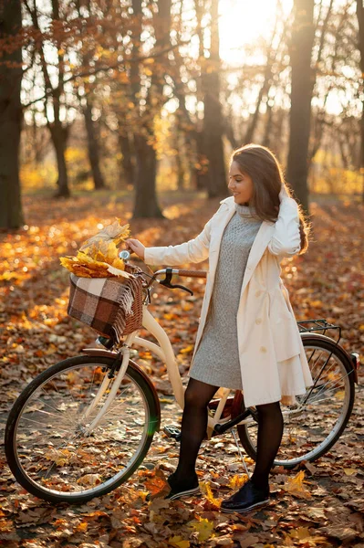 秋の公園で自転車で歩く幸せなアクティブな女性の垂直方向のビュー コートでリラックスして幸せな若い女の子 健康的なライフスタイルとレクリエーションレジャー活動のコンセプト — ストック写真