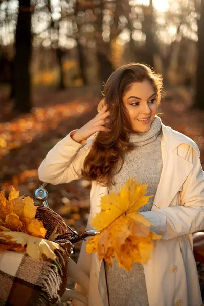 秋の森の中で自転車を眺めている若い女性 秋の大自然の中で都会の自転車と立ちながら笑顔でカジュアル服に積極的な女性 — ストック写真